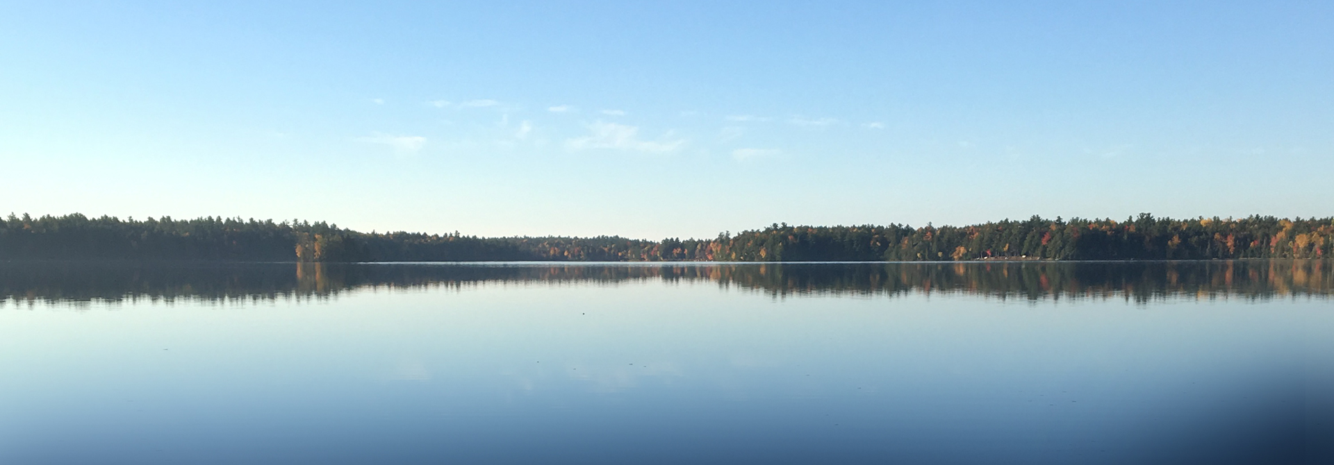 Fall lake in Maine, still water reflecting blue sky