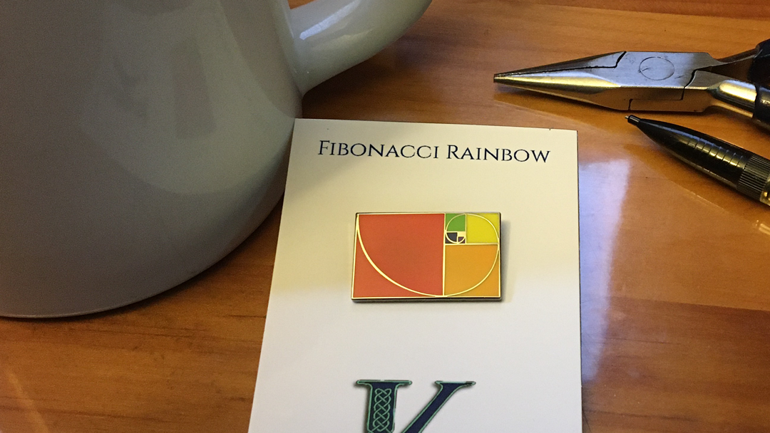 Fibonacci Rainbow pin on card on desk environment with mug, pencil, and pliers